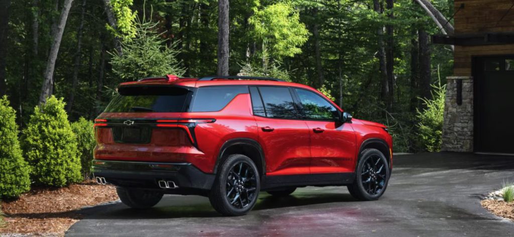 Image of a red Chevrolet Traverse SUV parked in front of a forest house