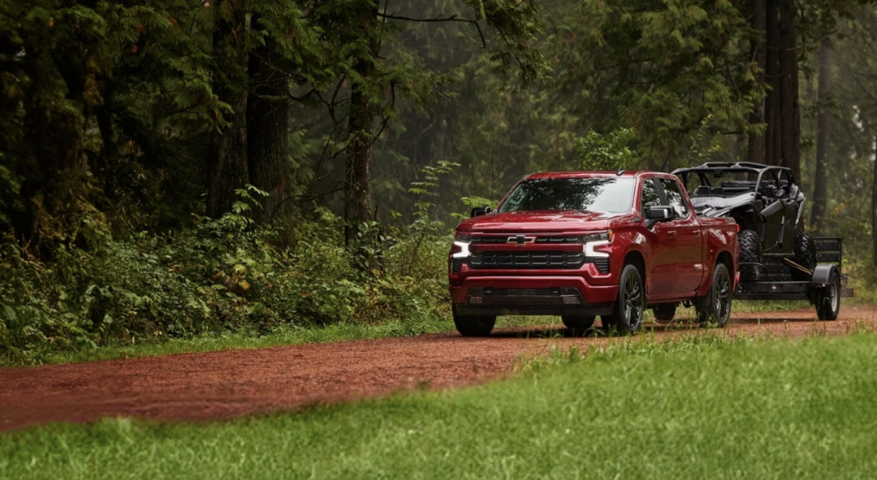 Red Chevrolet Silverado 1500 RST carrying a trailer with a razer on the back in the woods
