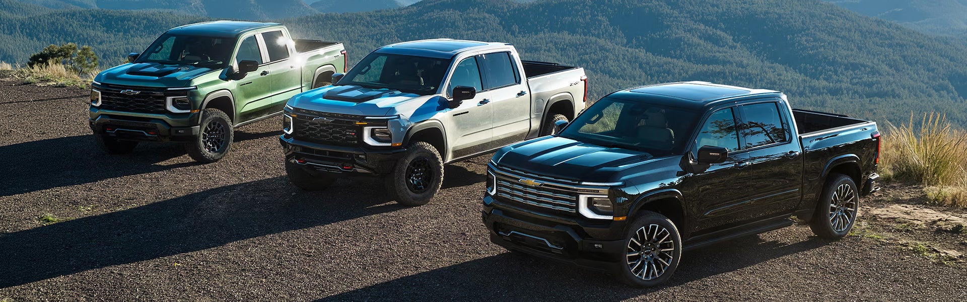 Green, white, and black 2027 Chevy Silverado 1500 pickups on a mountain overlook